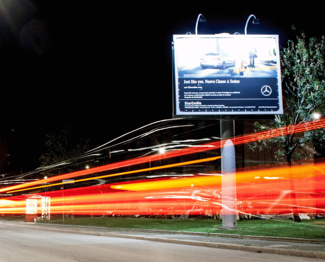 Vista notturna di un Poster Illuminato per Affissioni su una strada trafficata a Bologna